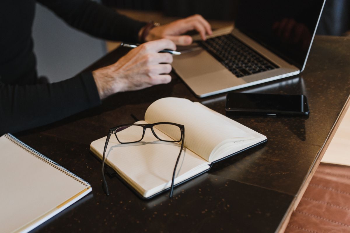 Mains sur un ordinateur portable, carnet et lunettes sur la table.